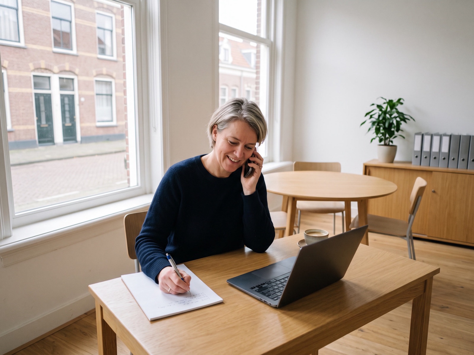 Een adviseur belt aan haar bureau op kantoor met een klant en maakt aantekeningen