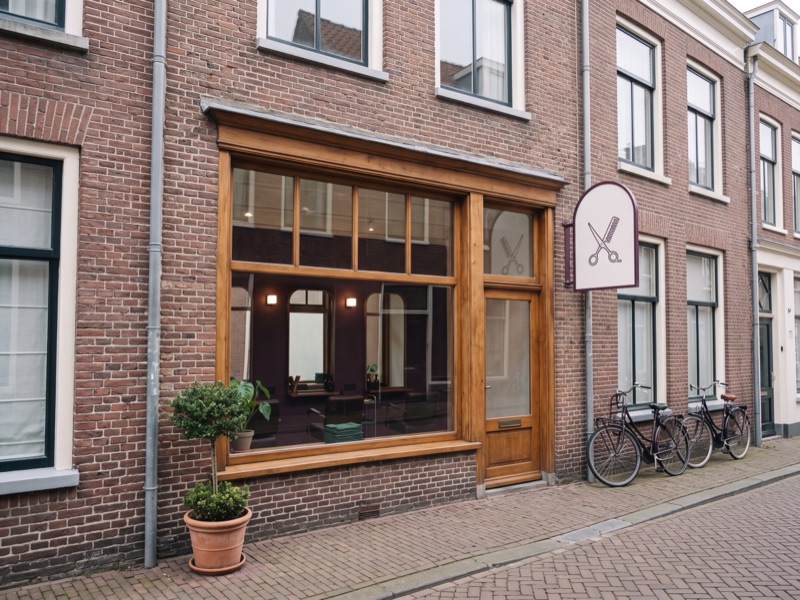 De gevel van de salon aan een winkelstraat, met een boogvormig bord met een schaar en een kam erop